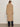 A person with long brown hair and glasses wears the Sanctuary Clothing "live in fur coat warm camel," paired with dark wide-leg jeans and black shoes, standing against a plain off-white wall.