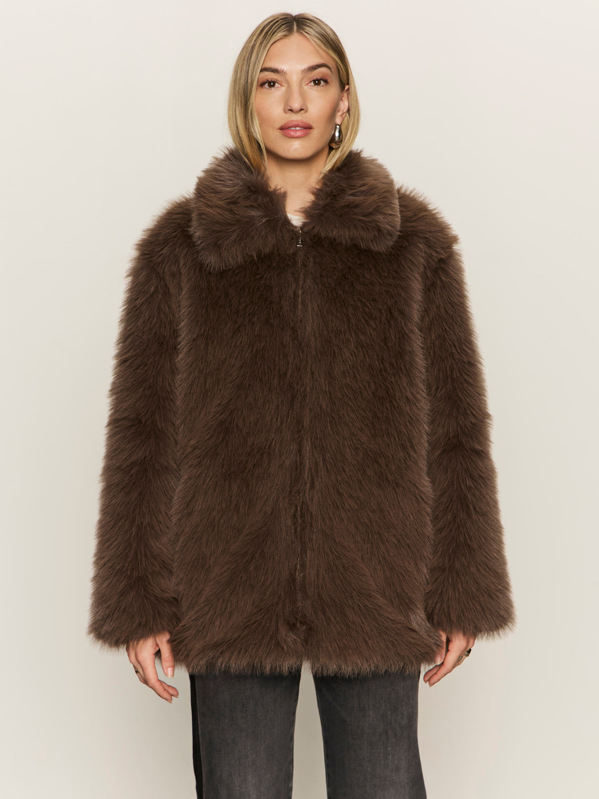 A person with straight blond hair wears the Sanctuary Clothing carmen fur coat morel and dark pants, standing against a plain light background.
