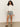 A woman with long curly hair wears the Sanctuary Clothing cropped paper boy jacket in bleached white, styled with blue striped shorts and black sandals, standing against a plain light wall with one hand in her pocket.