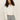 A woman with curly hair models the Sanctuary Clothing cropped paper boy jacket in bleached white, featuring a chest pocket, against a plain beige background.