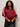A woman with curly hair models the Sanctuary Clothing satin track jacket in crimson (extended sizing), featuring white sleeve stripes. She pairs it with dark pants and a black studded purse, posing against a light background.