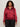 A woman with curly hair wears the Sanctuary Clothing satin track jacket in crimson (extended sizing) with white sleeve stripes and black pants, standing against a plain light background.