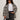 A woman wears the Sanctuary Clothing soiree barn jacket striking zebra (extended sizing) over a white tee and dark jeans, accessorized with black sunglasses, a belt, and handbag, standing against a plain light background.