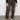 Wearing Sanctuary Clothing™s rebel pant hiker camo with a black textured long-sleeve top and white sneakers, the person stands against a plain wall, hands relaxed at their sides. Image cropped from chest down.