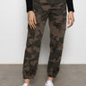 Wearing Sanctuary Clothing™s rebel pant hiker camo with a black textured long-sleeve top and white sneakers, the person stands against a plain wall, hands relaxed at their sides. Image cropped from chest down.