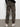 A person wearing Sanctuary Clothing rebel pant hiker camo, featuring side and back pockets with elastic ankle cuffs, and white sneakers stands facing a white wall, shown from the back.