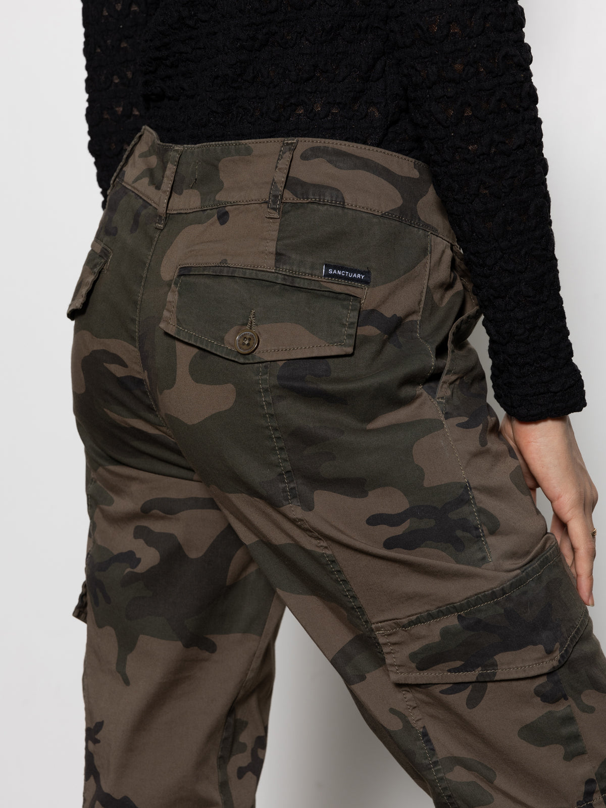 A person wearing the rebel pant hiker camo by Sanctuary Clothing, shown waist down and slightly turned to the side, rests one hand on their hip.