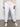 A person indoors wears Sanctuary Clothing's rebel pant brilliant white inclusive collection; only the lower body is shown against a neutral background.