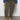 A person in Sanctuary Clothing's rebel pant hiker green (inclusive collection), a blue long-sleeve top, and white sneakers stands on a gray floor against a white wall. The photo is cropped just below the shoulders.
