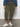 A person in Sanctuary Clothing's rebel pant hiker green (inclusive collection), a blue long-sleeve top, and white sneakers stands on a gray floor against a white wall. The photo is cropped just below the shoulders.