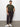 A woman stands against a white wall, wearing Sanctuary Clothing™s rebel pant obsidian from the inclusive collection with a green camo tee and white sneakers. Hands in her pockets, she looks confidently at the camera.