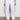 A person wearing Sanctuary Clothing's rebel pant in brilliant white, paired with white sneakers and a black top. Only the lower half of the body is visible, standing against a plain light-colored wall.
