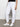 A person wearing Sanctuary Clothing's rebel pant in brilliant white stands on a gray floor against a plain white background, showing only the lower half of the body. White sneakers with beige accents and a black top complete the look.