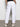 A person wearing Sanctuary Clothing's rebel pant in brilliant white, featuring side and back pockets, paired with a black top and white sneakers, stands with their back to the camera against a plain background.