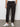 Wearing a white t-shirt, white sneakers, and Sanctuary Clothing's rebel pant obsidian cargo pants with elastic cuffs, a person stands against a plain, light-colored wall with hands in pockets.