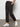 A person stands indoors with hands in pockets, modeling the Sanctuary Clothing rebel pant obsidian”black cargo pants with side pockets”paired with white sneakers. Only the lower half of their body is visible against a plain background.