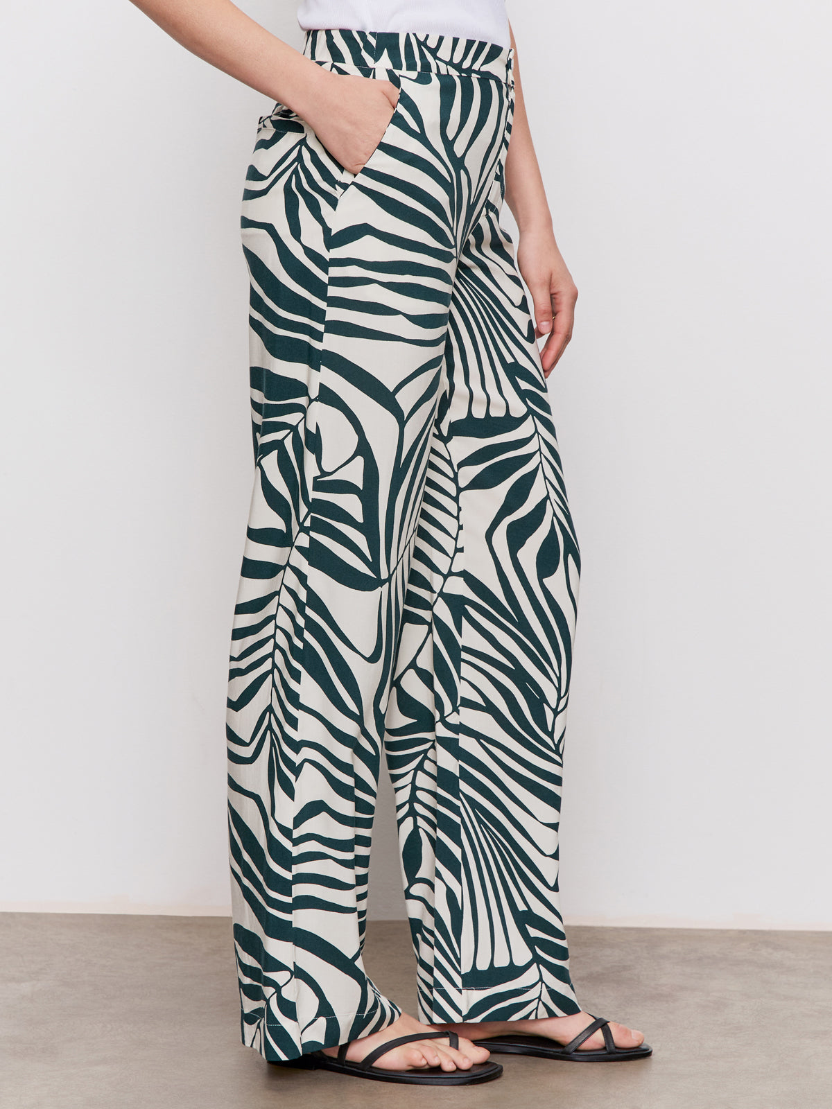 A person wears Sanctuary Clothing’s “the soft trouser green oasis”—high-waisted, wide-leg green pants—paired with a white top and black sandals, standing against a plain background.