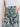 A person wears the Sanctuary Clothing "the soft trouser green oasis," featuring a bold green and white leaf print, paired with a sleeveless white top. One hand is in the pocket, and part of the arm and torso are shown.