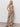 A woman with long, wavy blond hair and a relaxed expression wears Sanctuary Clothing„s œthe soft trouser desert bandana��a sleeveless, loose beige jumpsuit with a dark brown paisley pattern�and black sandals against a plain backdrop.