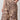 A person wearing Sanctuary Clothing's "the soft trouser desert bandana"—beige pants with a dark brown paisley and floral print—stands with one hand in their pocket, showing only the lower torso and upper legs.