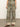 A person wearing "The Soft Trouser Mezzo Sage" by Sanctuary Clothing, featuring a high-waisted, wide-leg style in an intricate green and brown paisley pattern with a wide hem showcasing a smaller geometric design, paired with brown sandals.