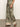 A person is standing on a smooth gray floor wearing brown sandals and "The Soft Trouser Mezzo Sage" from Sanctuary Clothing, featuring a high-waisted, wide-leg design with a green and beige floral and paisley pattern. Their upper body is not visible.