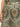 Close-up of someone wearing "the soft trouser mezzo sage" by Sanctuary Clothing, featuring intricate floral and paisley designs in green, orange, and beige. The left hand rests near the hip, with a single button visible at the waistband.