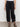 Wearing Sanctuary Clothing's cali cargo pant black, which features multiple pockets and adjustable ankle straps, paired with black sandals and a white top, a person stands against a plain light background.