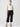 A person with long hair in a ponytail is wearing a white short-sleeved shirt, black Cali Cargo Pant Black by Sanctuary Clothing rolled up at the cuffs, and black sandals. They are standing against a plain, light-colored background and looking directly at the camera.