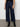 A person wears Sanctuary Clothing's the marine magnetic wide-leg, dark blue jeans with front patch pockets, paired with a black top and black ankle boots, standing against a light-colored wall and concrete floor.