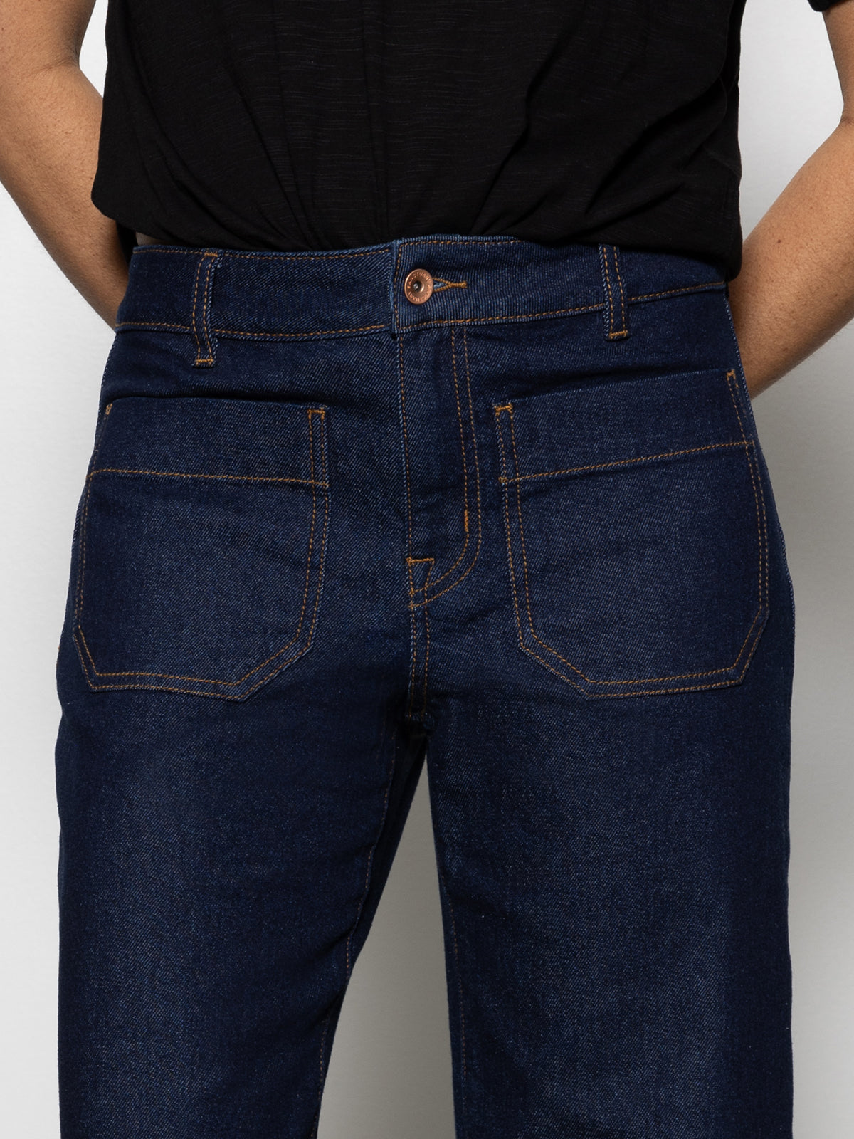 A person wears Sanctuary Clothing's the marine magnetic high-waisted dark blue denim jeans with orange stitching and a black shirt, standing against a plain light background. The cropped image shows only the torso and upper legs.