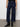 A person wears Sanctuary Clothing's the marine magnetic dark blue wide-leg jeans with front pockets, paired with a black top and black ankle boots, standing against a plain light background.
