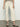 A person wears Sanctuary Clothing's "the marine crop trouser pant" in French Vanilla, paired with a striped shirt and snake-patterned crisscross sandals, while standing on a concrete floor. The top of the person is cropped from the image.