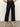 A person wearing Sanctuary Clothing's the marine jeans after hours�high-waisted, wide-leg black jeans with front pockets�paired with a leopard print top and beige heeled ankle boots stands against a plain background.
