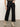 Wearing Sanctuary Clothing's the marine jeans after hours, a person stands against a plain background with one hand in a pocket, styled with light beige ankle boots and a leopard print top.