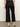 A person faces away, wearing Sanctuary Clothing's the marine jeans after hours�dark wide-leg denim�with a leopard print top and light beige heeled boots against a plain, light-colored wall and floor.