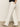 A person showcases their side profile in marine full length semi high rise jeans bleached white by Sanctuary Clothing, paired with black heeled sandals against a plain background, where only the neck to feet are visible.