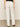 A person wears Sanctuary Clothing's marine full length semi high rise jeans in bleached white, featuring back pockets and straight legs, paired with a black top. They stand on a beige floor against an off-white background.