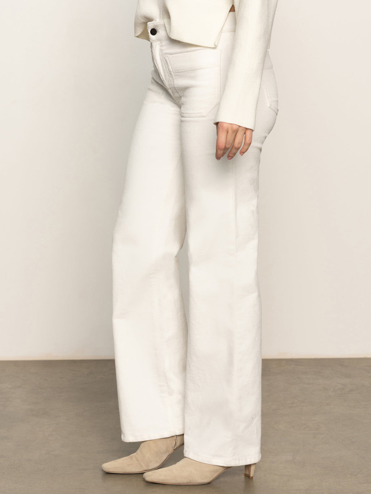 The lower half of a person is shown against a neutral background, wearing Sanctuary Clothing's corduroy marine pant in chalk with a cream top and beige pointed-toe heels.