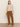 A woman stands against a plain background wearing Sanctuary Clothing's corduroy marine pant in bronze with a loose beige long-sleeve top and cream heeled boots, looking forward with a neutral expression.