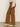 Someone stands on a smooth concrete floor against a plain light wall wearing Sanctuary Clothing's corduroy marine pant in bronze, paired with a beige long-sleeve top and cream heeled ankle boots.