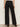 A person faces away wearing the Sanctuary Clothing runway ponte trouser in black—high-waisted, wide-leg pants with two back welt pockets, paired with black heeled shoes. The look is set against a plain, light-colored background.