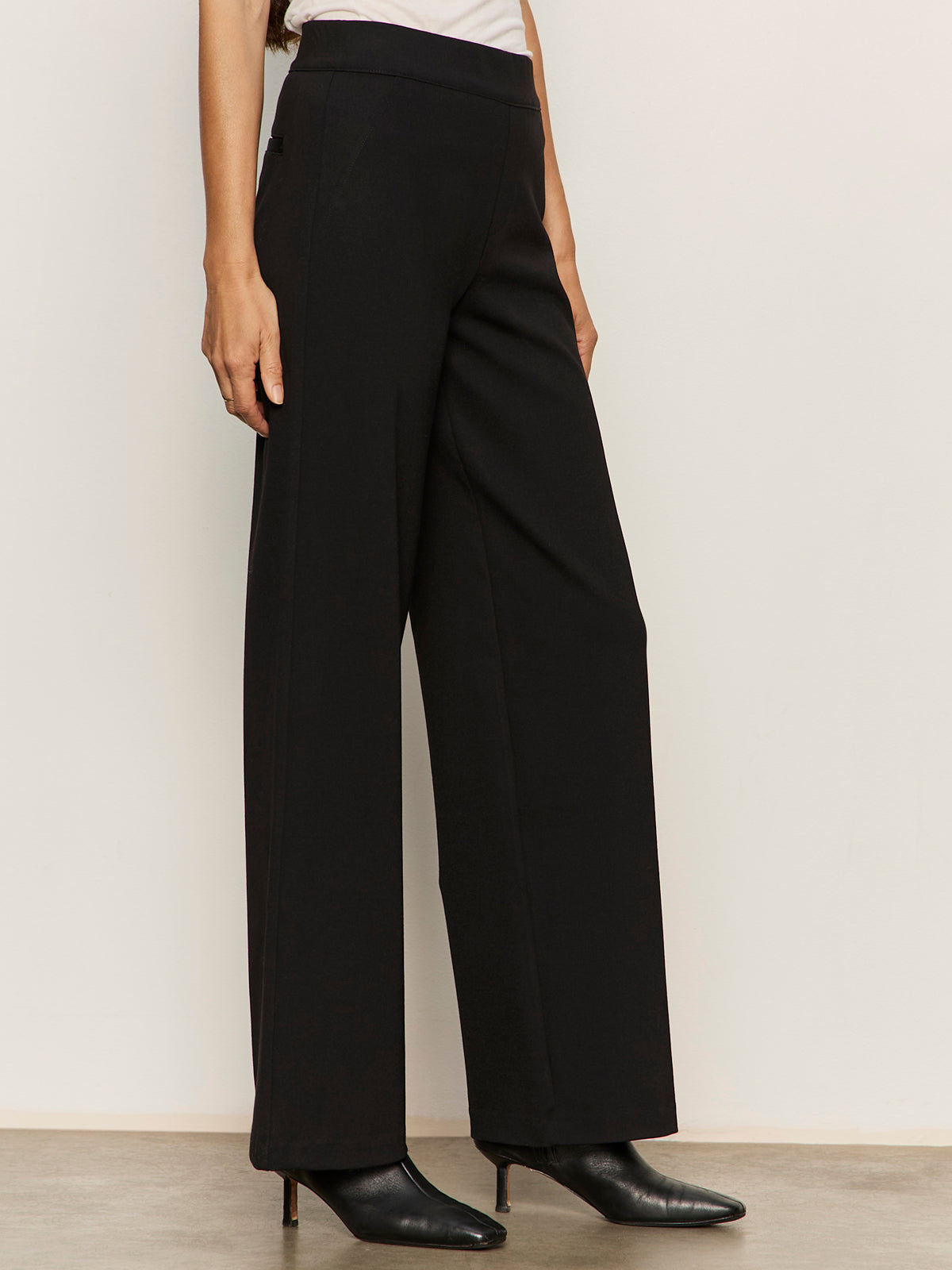 A person wearing Sanctuary Clothing’s runway ponte trouser in black with black heeled boots, standing against a plain light wall. Only the lower half of their body is visible.