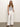 Against a plain background, a person is casually posed with one hand in their pocket. They have long hair and wear a sleeveless black and white striped top, arden wide leg jeans brilliant white by Sanctuary Clothing, and black sandals.