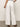 A person stands with their back to the camera wearing Sanctuary Clothing's arden wide leg jeans in brilliant white paired with a black and white striped top, one hand relaxed by their side. They wear sandals on a gray floor, set against a plain backdrop.