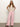 A woman stands confidently in Sanctuary Clothing's arden wide leg jeans washed cherry blossom and a sleeveless white crochet top, with long brown hair and dark sandals against a plain, light-colored wall.