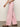 A person wearing Sanctuary Clothing's Arden wide-leg jeans in washed cherry blossom and brown sandals, paired with a white textured top, walks in a side view from the torso down against a plain background.