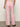 A person stands facing away, wearing Sanctuary Clothing's high-waisted Arden Wide Leg Jeans in Washed Cherry Blossom and a white textured top. They have a bracelet on one wrist and open-toed brown sandals against a plain white wall.