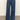 A person models Sanctuary Clothing's arden wide leg jeans in the shade perfect storm, standing with hands in pockets and paired with brown sandals against a plain background.