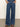 A person models Sanctuary Clothing's arden wide leg jeans in the shade perfect storm, standing with hands in pockets and paired with brown sandals against a plain background.